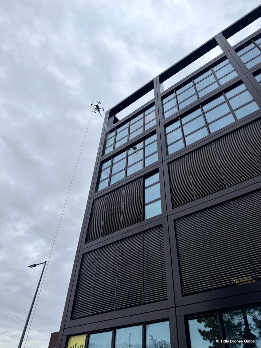 Drohen fliegt entlang der Hausfassade und reinigt dabei die Fenster einer Schule | © Tidly Drones
