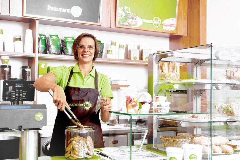 Gut gelaunte Deli-Mitarbeiterin bei der Ausgabe von Waren. 