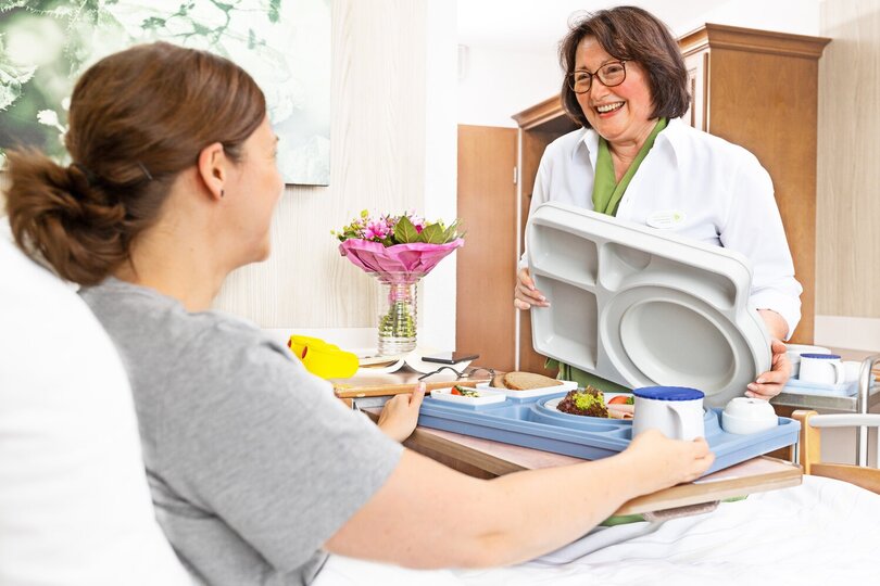 Pflegekraft serviert Essen am Krankenbett