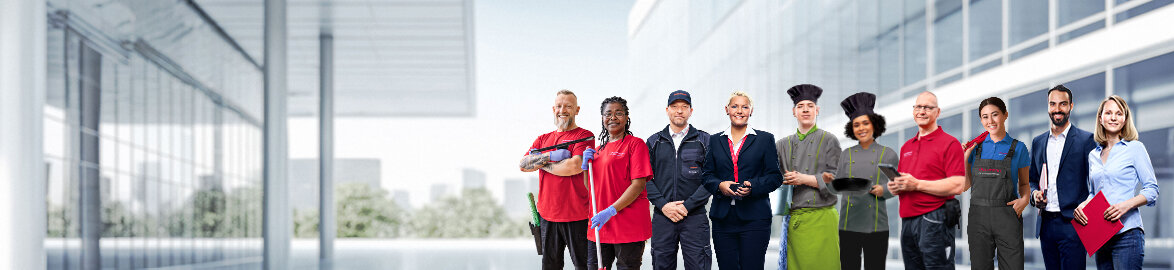 Gruppenbild von lächelnden Dussmann-Mitarbeitenden aus unterschiedlichen Arbeitsbereichen vor neutralem grauem Hintergrund. 