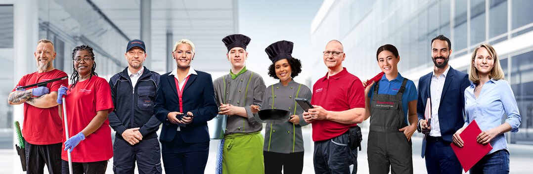 Gruppenbild von lächelnden Dussmann-Mitarbeitenden aus unterschiedlichen Arbeitsbereichen vor grauem Hintergrund, die ihre Arbeitskleidung tragen. 
